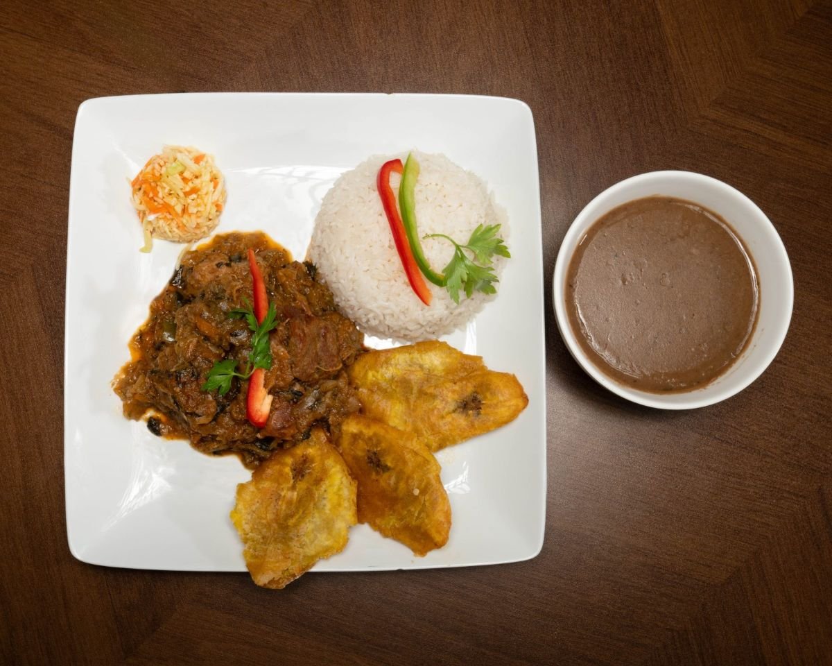Haitian legim with white rice, fried plantains, pikliz, and a side of creamy bean sauce