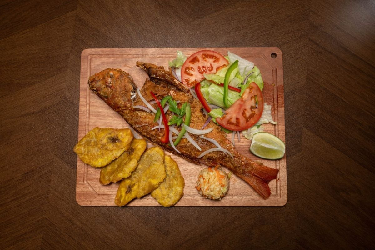 Whole Haitian fried fish with fried plantains, fresh salad, lime, and pikliz