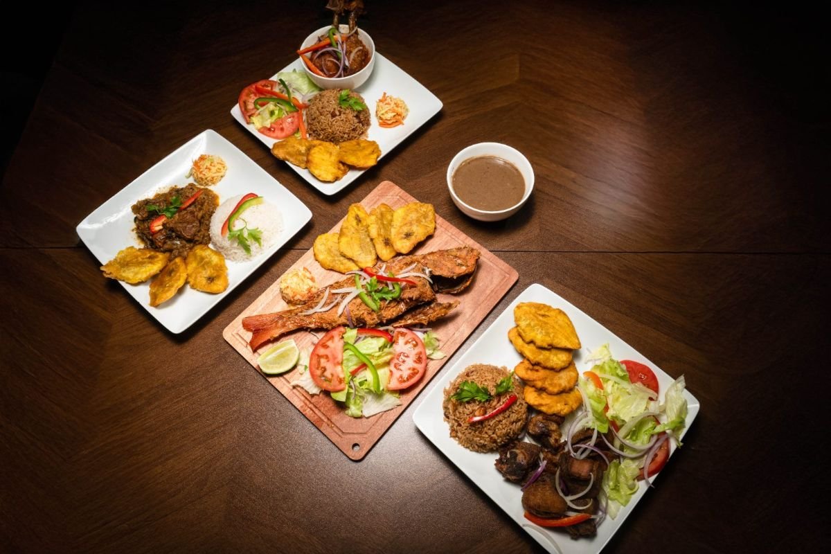 A spread of Haitian favorites including griot, legim, fried fish, rice, plantains, pikliz, and bean sauce